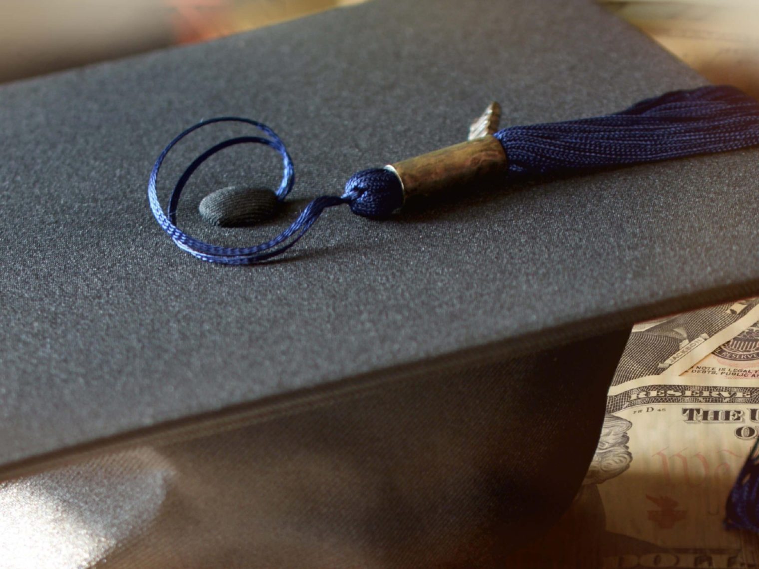 Student mortar board on a pile of cash.