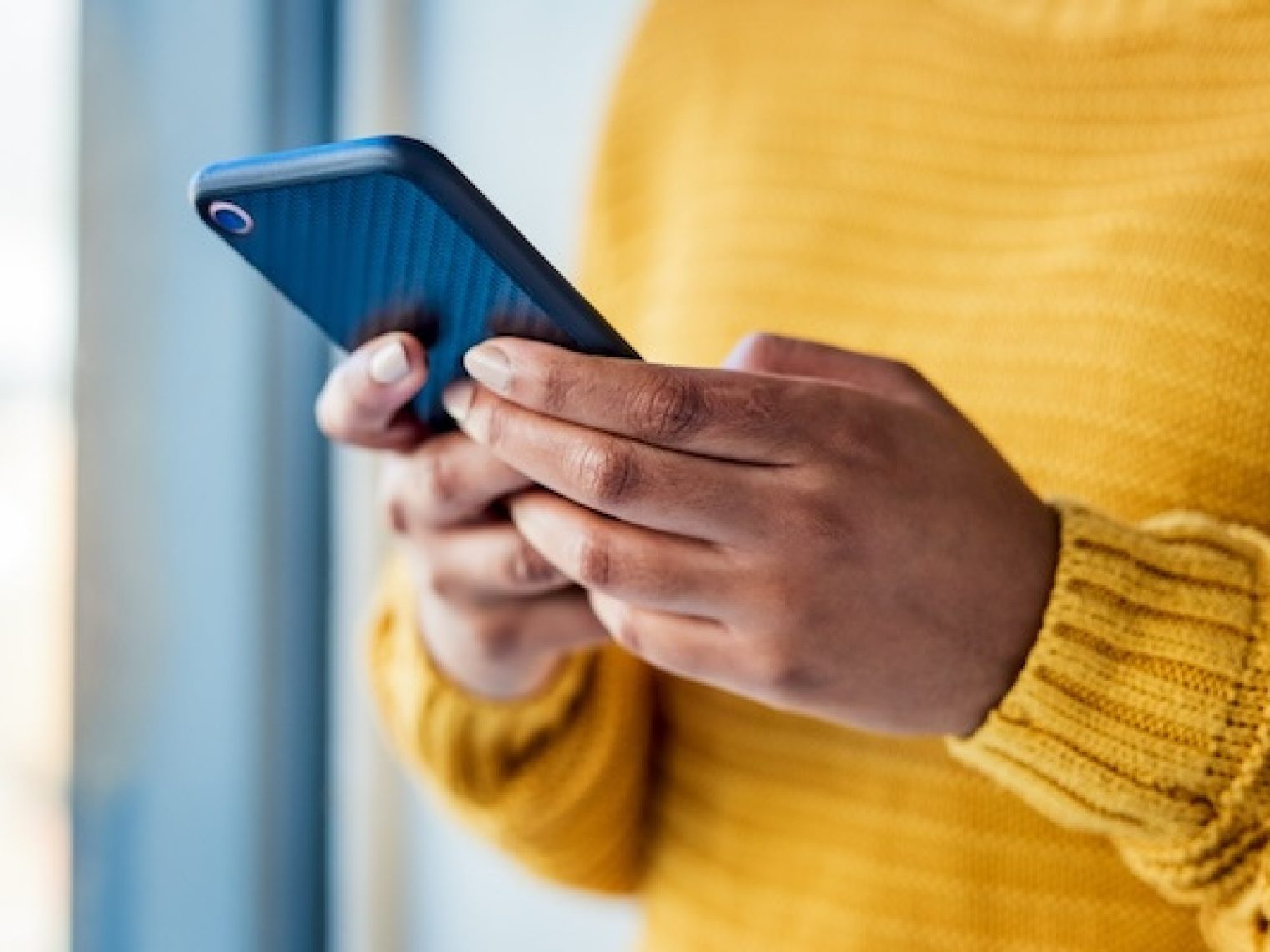 Photo of an unrecognizable woman using a mobile phone indoors.